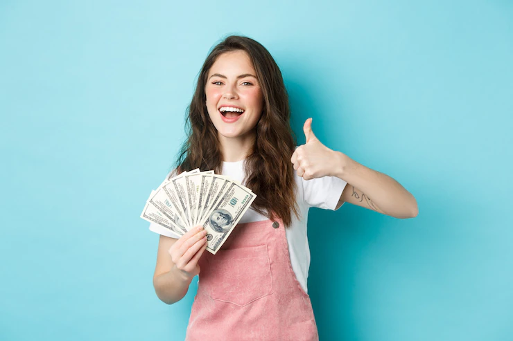 smiling happy woman holding money dollar bills showing thumb up recommending fast cash loan looking satisfied standing blue background 1258 70119